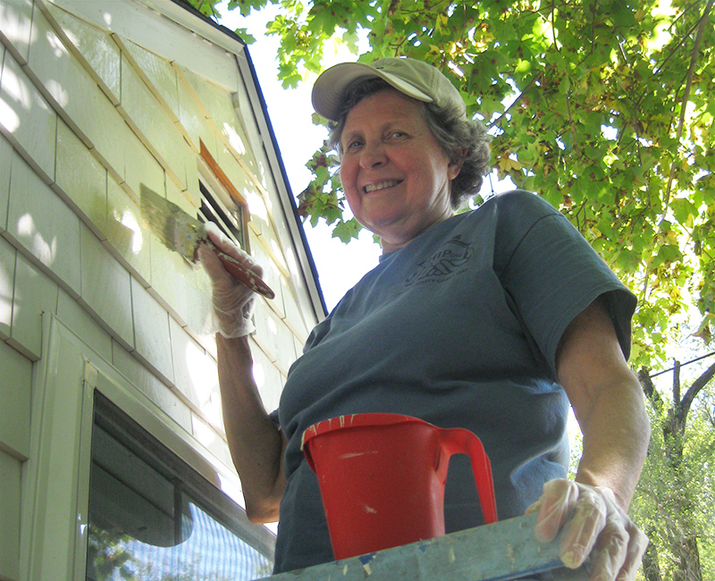 woman painting the siding of a house
